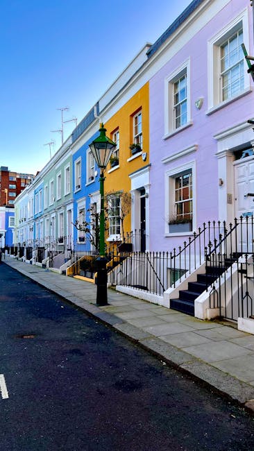 A row of brightly painted terraced houses along a residential street in Kensington, featuring pastel shades of blue, yellow, and lavender. The houses have white-framed sash windows, black wrought iron