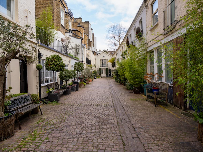 A quiet cobbled street in a residential and commercial area with Victorian-style brick buildings, including a prominent red-brick facade on the left with a sign for a business named 'HEZZO' visible on